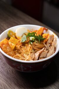 Close-up of curry mee with noodles, chicken, tofu, and boiled egg in a rich spicy broth.